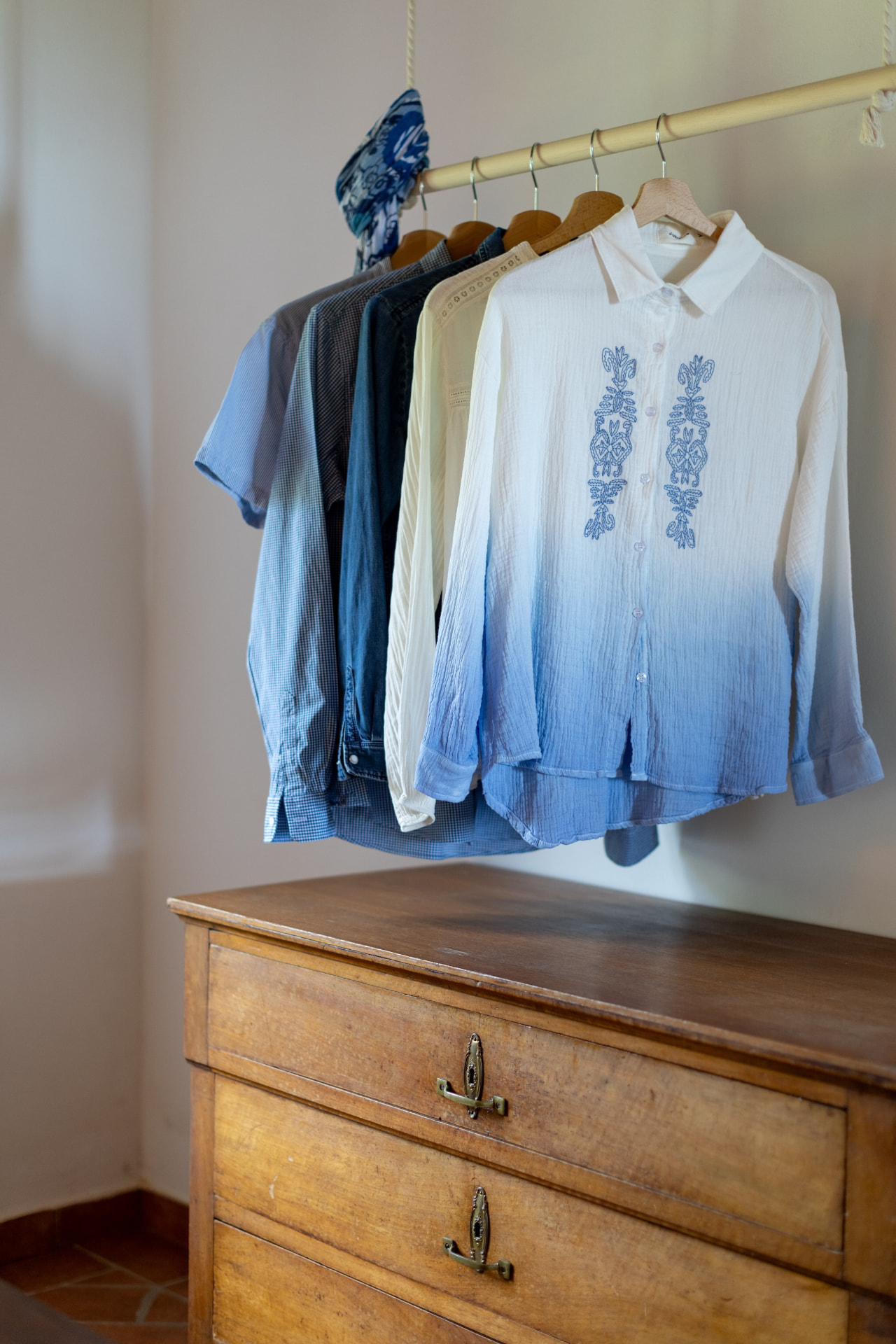 Shirts on wooden hangers above an antique chest of drawers