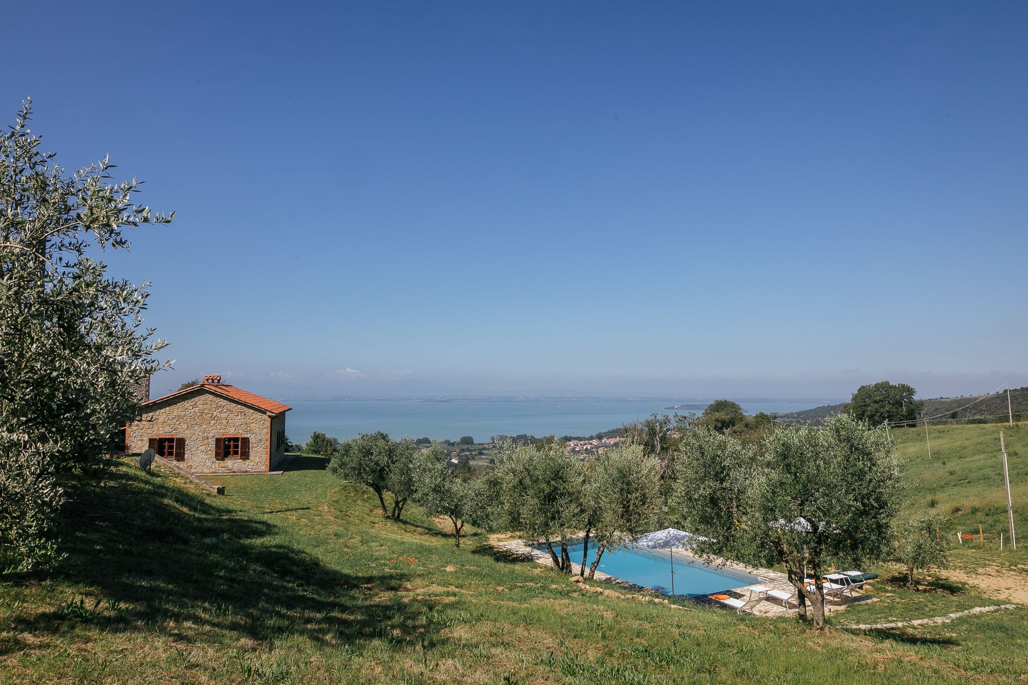 Casa Campori, a private villa in Umbria, seen across olive groves with Lake Trasimeno behind