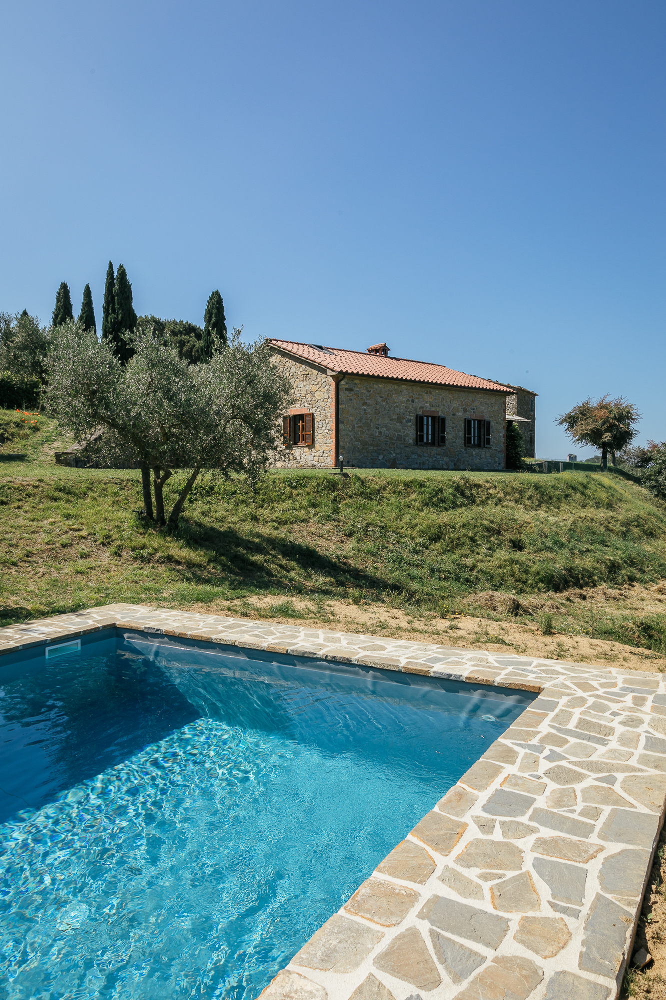 View across the pool to the stone house under a clear sky
