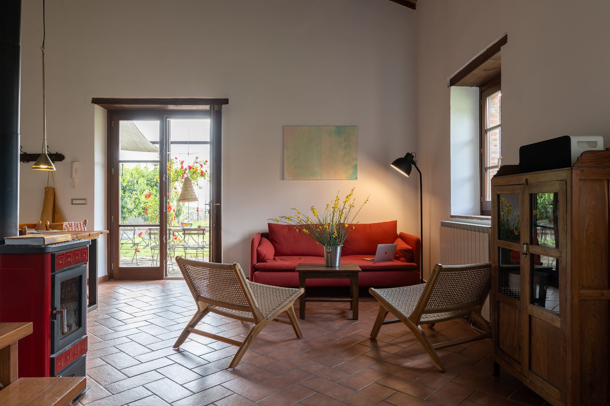 Sitting room with red stove, armchairs and terracotta floor